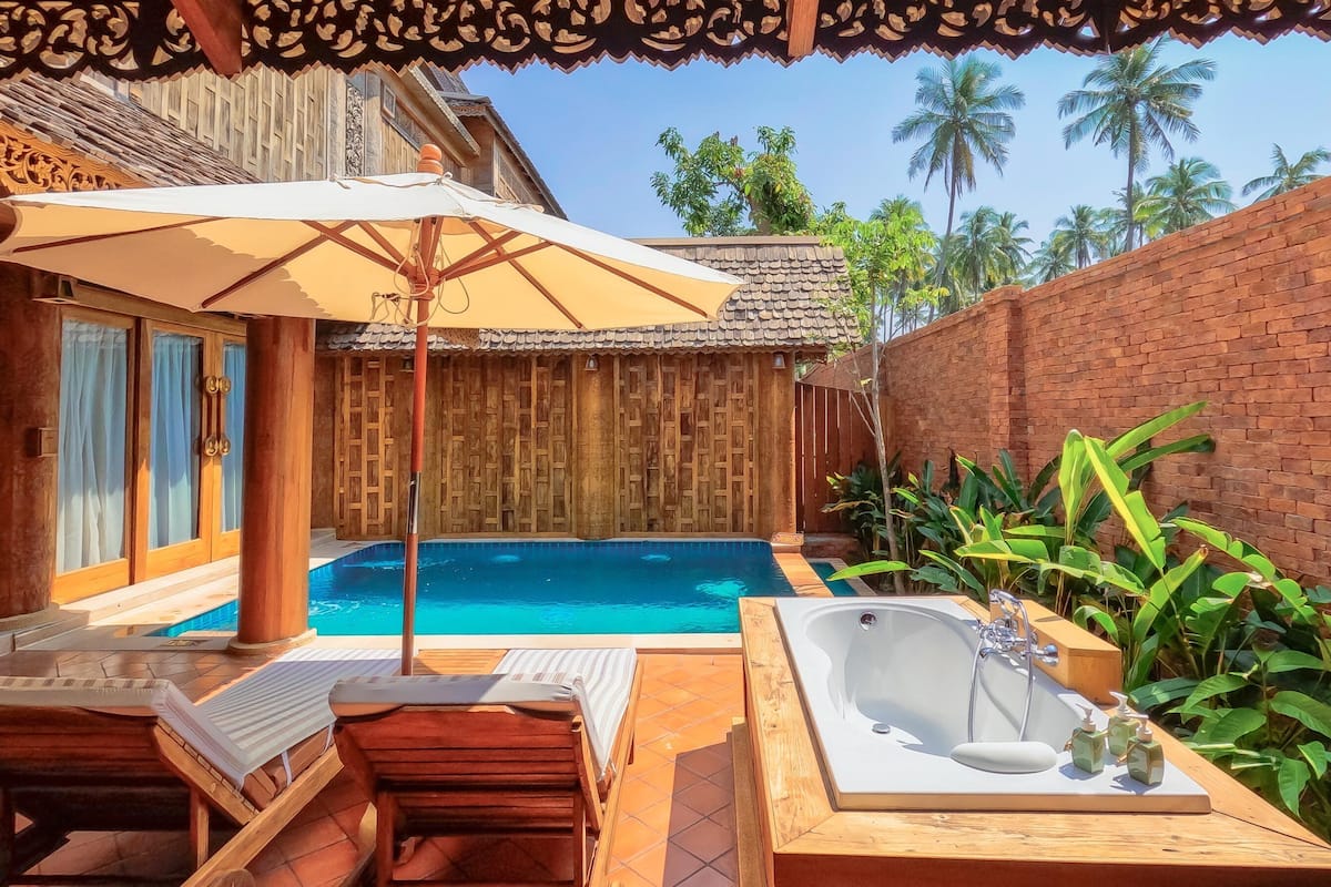A pool area with a hot tub, lounge chairs, and a wooden fence.