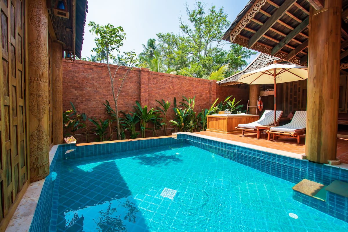 A swimming pool with tiled edges, surrounded by a brick wall and wooden pillars.