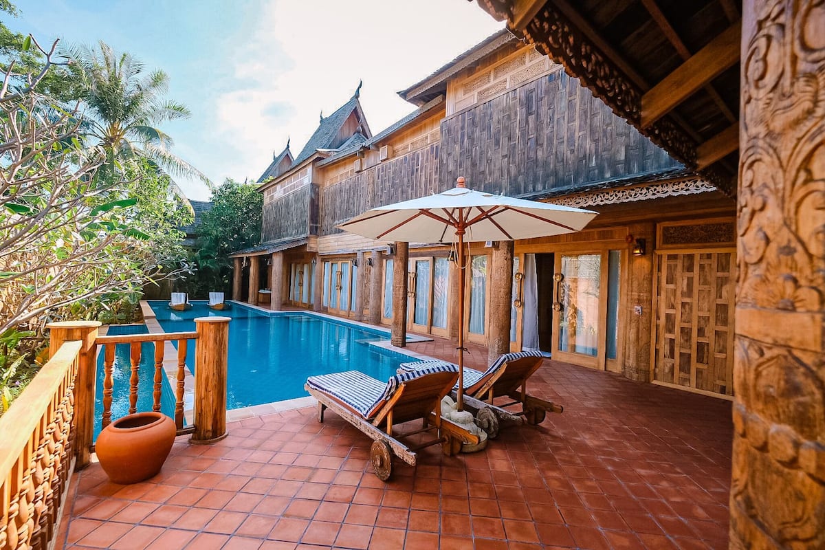A wooden building with a swimming pool, two sun loungers, and a large umbrella.