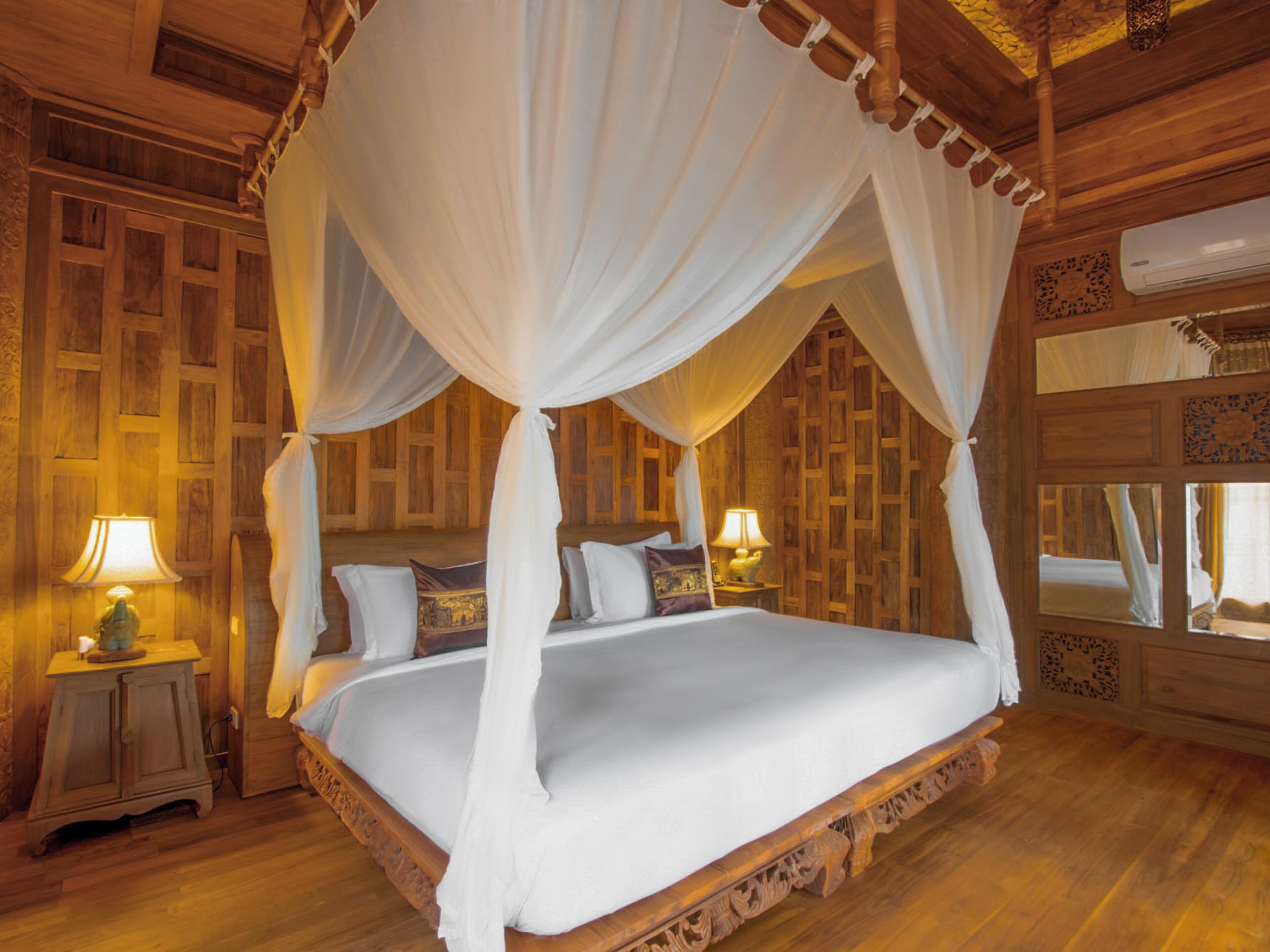 A four-poster canopy bed with white linens, wooden paneling on the walls, and a wooden floor.