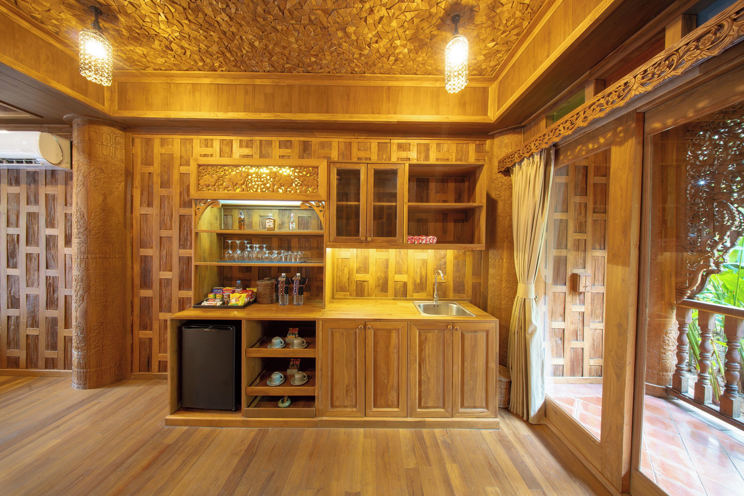A wooden kitchen with a built-in refrigerator, shelves with bottles, and a window with curtains.