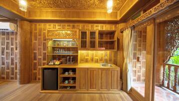 A wooden kitchen with a built-in refrigerator, shelves with bottles, and a window with curtains.