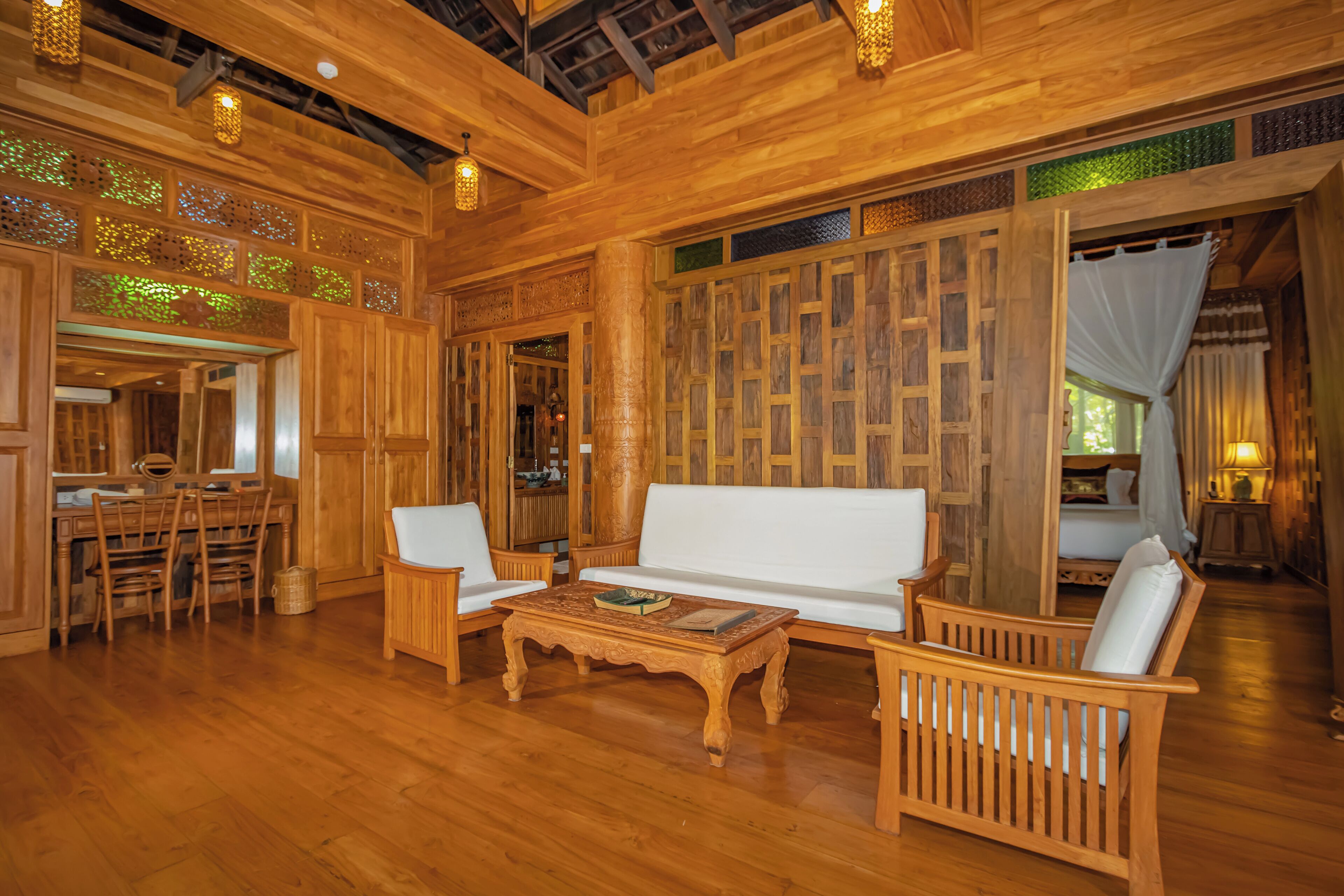 Une pièce au plancher de bois, avec un canapé blanc, deux chaises en bois, une table basse en bois et un coin repas comprenant des chaises et une table en bois.