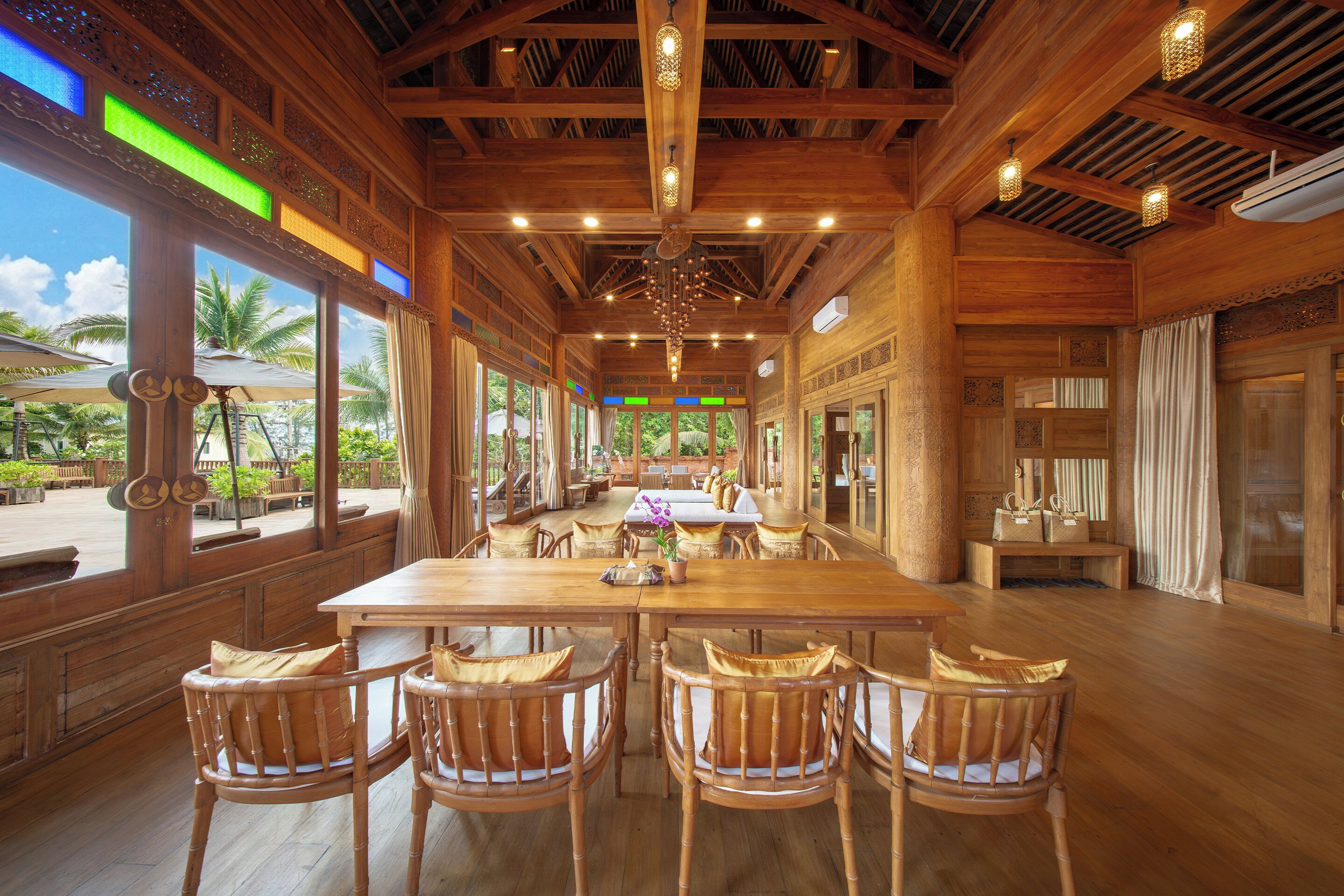 A spacious wooden dining area with a long table and chairs, large windows with curtains, and a view of the outdoors.