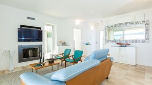 A modern living room with a sofa, chairs, a fireplace, a TV, and a kitchen area. - Villa Amar 4, Emma Villas (Pittulongu)