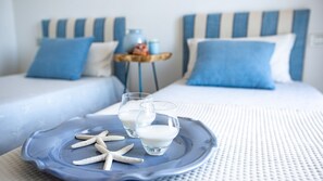 En pænt redt seng med blå og hvide stribede sengegavl og puder, et bakke med stjerneskaller og glas med mælk, og et lille bord med en vase og pynteting.