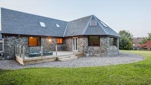 Een stenen huis met een schuin dak, een houten terras en een klein voortuintje.