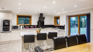 Een moderne keuken met een centraal eiland, barkrukken en een eettafel.