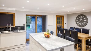 Een moderne keuken met een marmeren eiland, een schaal met fruit en een eethoek met een houten tafel en stoelen.