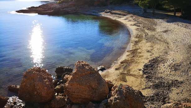 A beach with clear water, rocky formations, and a forested area in the background.
