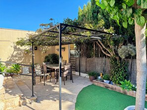 A patio with a pergola, a table with chairs, and a small artificial green lawn.