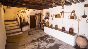 A rustic interior with a stone staircase, a shelf with pottery, and a wooden ceiling.