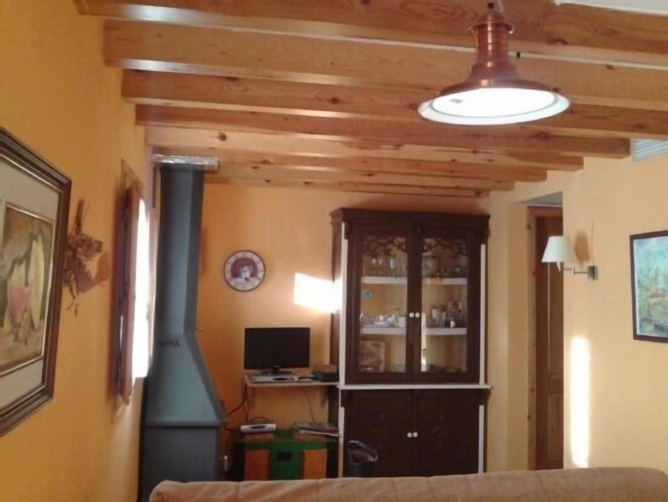 A room with wooden ceiling beams, a fireplace, a cabinet with glass doors, and a television.