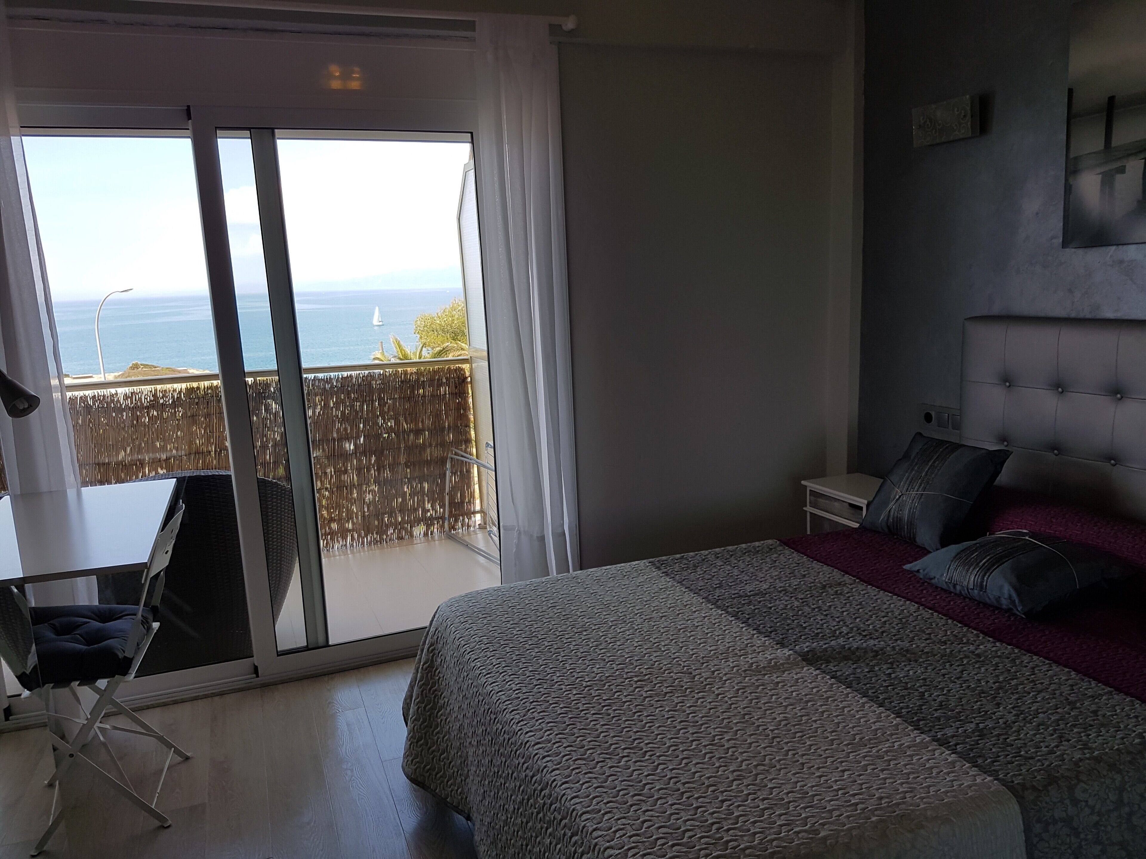 Een slaapkamer met een bed, een bureau en uitzicht op de zee door een schuifdeur.