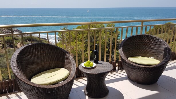 A balcony with wicker furniture, a small table with a bottle and fruit, and a view of the sea. - Apartment facing the sea with pool and 2 bedrooms (Salou)