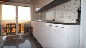 A modern kitchen with white cabinets, a Bosch dishwasher, and a glass door leading to a balcony with outdoor seating. - Apartment facing the sea with pool and 2 bedrooms (Salou)
