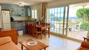 A spacious living area with a dining table and chairs, a sofa, and a kitchen in the background. - Villenpark Playa Arena House Bequia (Lloret de Mar)