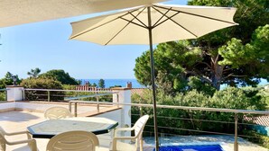 A patio with a table and chairs, a pool, and a view of the sea. - Villenpark Playa Arena House Bequia (Lloret de Mar)