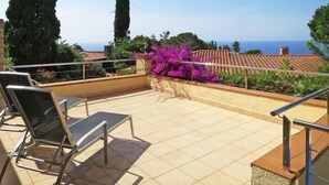 A balcony with a view of the sea, a pergola with purple flowers, and a tiled floor. - Villenpark Playa Arena House Bequia (Lloret de Mar)