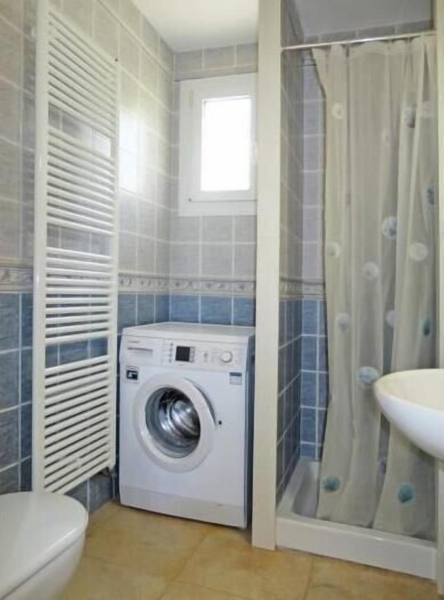 A compact laundry room with a washing machine, a radiator, and a shower area.