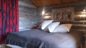 A log cabin room with a bed, a red and black patterned curtain, and a wall mural. - Kivikoski riverside cottage in Pyhtää for 5-8 people (Pyhtää)
