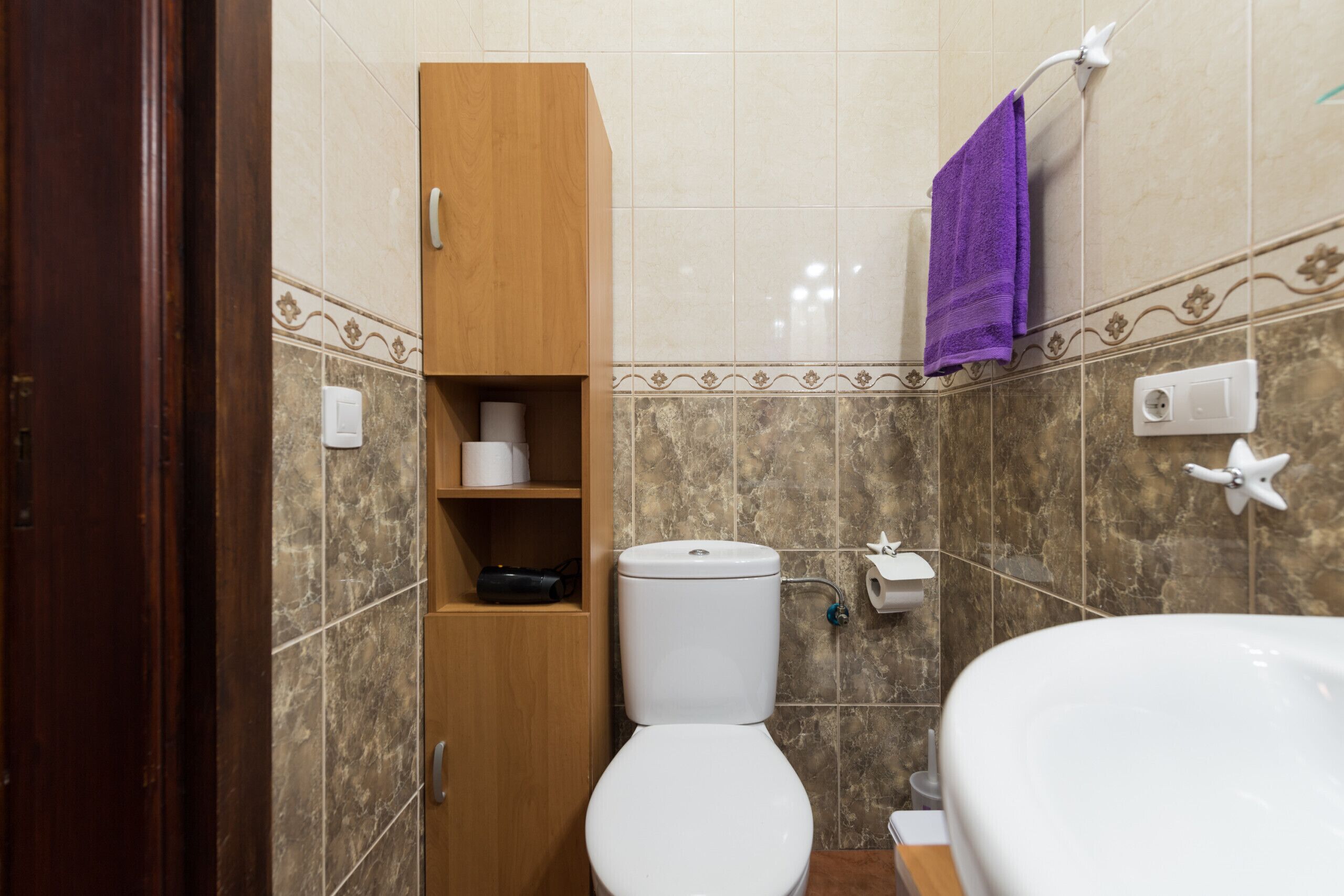 Une salle de bain équipée de toilettes, d’un lavabo et d’un meuble en bois avec des étagères.