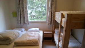 A dormitory room with bunk beds, a window with curtains, and a small bedside table. - Detached chalet on the slopes and near the village, for winter sports & summer holidays (La Norma)