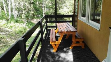 Une table de pique-nique en bois, posée sur un balcon, recouverte d’un tapis en caoutchouc noir et entourée d’une rambarde en métal noir, d’où l’on peut admirer une zone boisée.