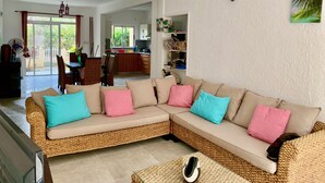 Una sala de estar con un amplio sofá modular tejido, una mesa de centro y una zona de comedor con mesa y sillas.