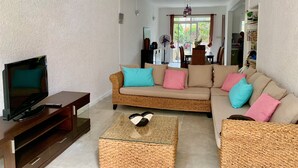 Una sala de estar con televisor, sofá de mimbre y una mesa de centro de vidrio.