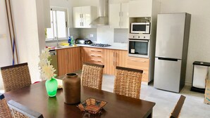 Una cocina moderna con armarios de madera, un refrigerador de acero inoxidable y un comedor con sillas de mimbre y una mesa de madera.