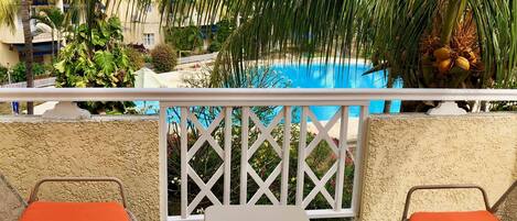 Ein Balkon mit Blick auf einen Pool, zwei orangefarbene Sitzgelegenheiten und ein weißer Tisch.