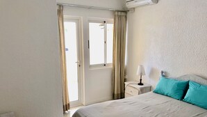 Un dormitorio con cama, mesita de noche, lámpara y ventana con cortinas.