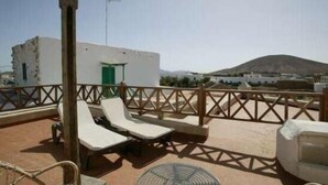 Terraço no telhado com duas cadeiras de descanso, um pequeno edifício com porta verde e uma montanha ao fundo.