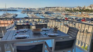 Een eettafel op een balkon, met uitzicht op een jachthaven en stadsbeeld.