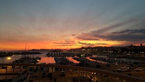 Een jachthaven in de zonsondergang met aangemeerde boten, een brug en een stadsgezicht op de achtergrond.