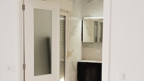 Une pièce avec une porte blanche donnant sur une salle de bain équipée d’un meuble-lavabo noir et d’un miroir.