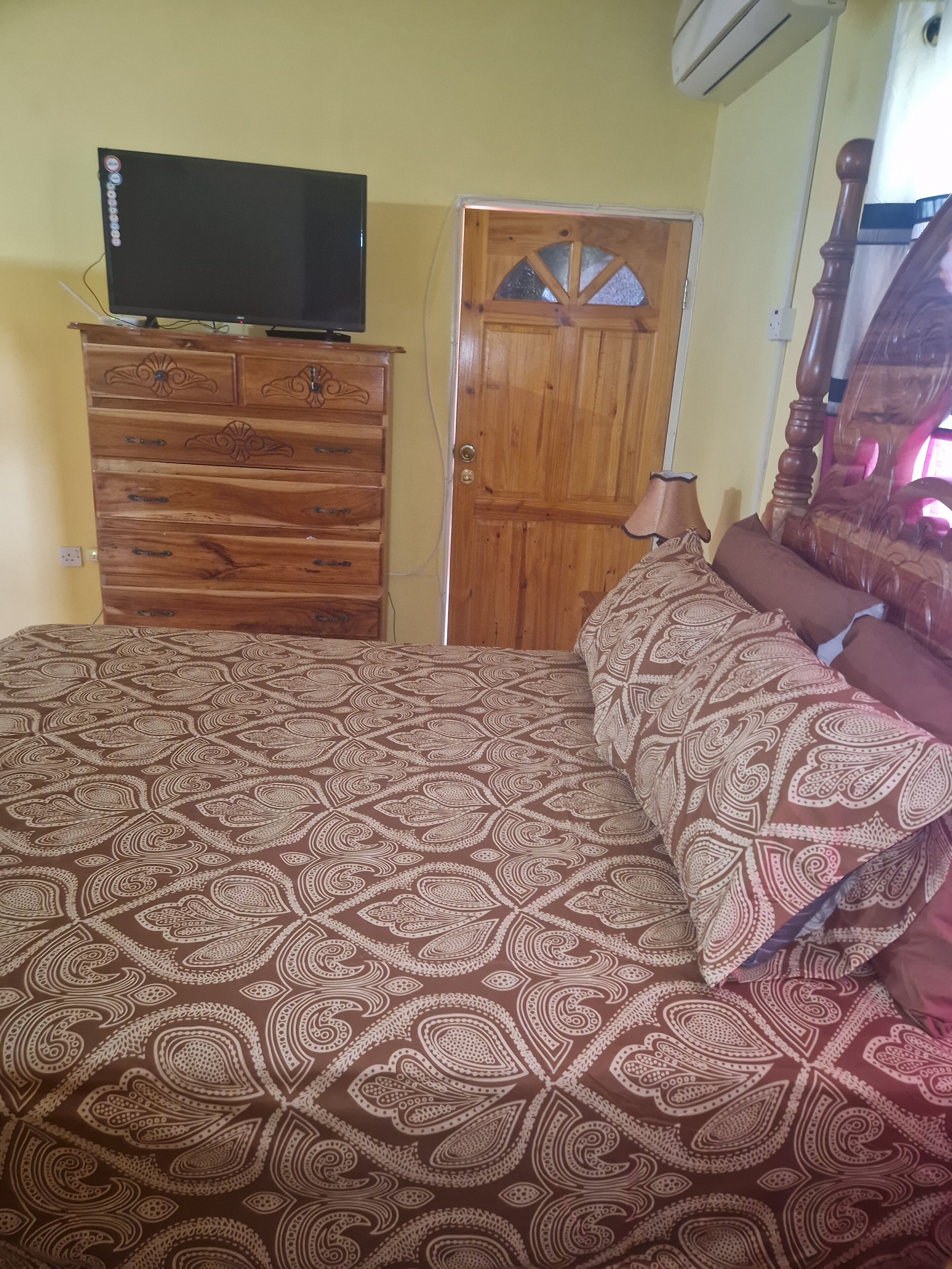 A bedroom with a bed, a wooden dresser, a television on top, and a wooden door.