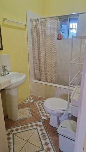 Ein kleines Badezimmer mit Toilette, Waschbecken, Duschvorhang und Fliesenboden.