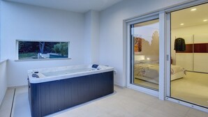 A modern bathroom with a large bathtub, a sliding glass door leading to a bedroom, and a window with a view of greenery. - Beautiful brand new villa ***** with heated swimming pool, summer kitchen, WiFi, grill (Pula)