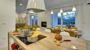 A modern kitchen with a wooden countertop, stainless steel pots, and a built-in stove. There is a dining area with yellow chairs and a large window. - Beautiful brand new villa ***** with heated swimming pool, summer kitchen, WiFi, grill (Pula)