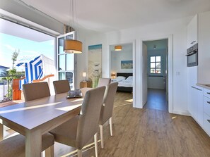 A modern hotel room with a wooden dining table, comfortable chairs, a bed with a view, and a kitchenette. - Comfortable 3-room apartment, sea view balcony and 200 m to the beach (Börgerende)