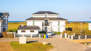 Une maison à deux étages avec un grand jardin devant, une allée et une vue sur l’océan.