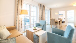 Une chambre d’hôtel moderne équipée d’un canapé, de fauteuils, d’une table à manger et de grandes fenêtres.