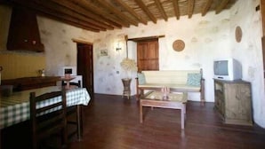 A rustic room with wooden beams on the ceiling, a dining table with a checkered tablecloth, a sofa, and a television on a wooden cabinet. - Tamasite Country House, Amanay (Tuineje)
