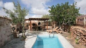 A swimming pool with lounge chairs and a pergola, surrounded by stone walls and trees. - Tamasite Country House, Amanay (Tuineje)