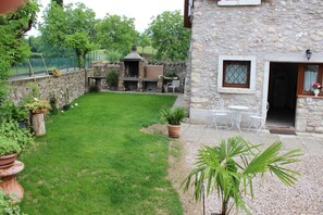 Enjoy al fresco dining on the patio surrounded by lush greenery and a charming stone structure.