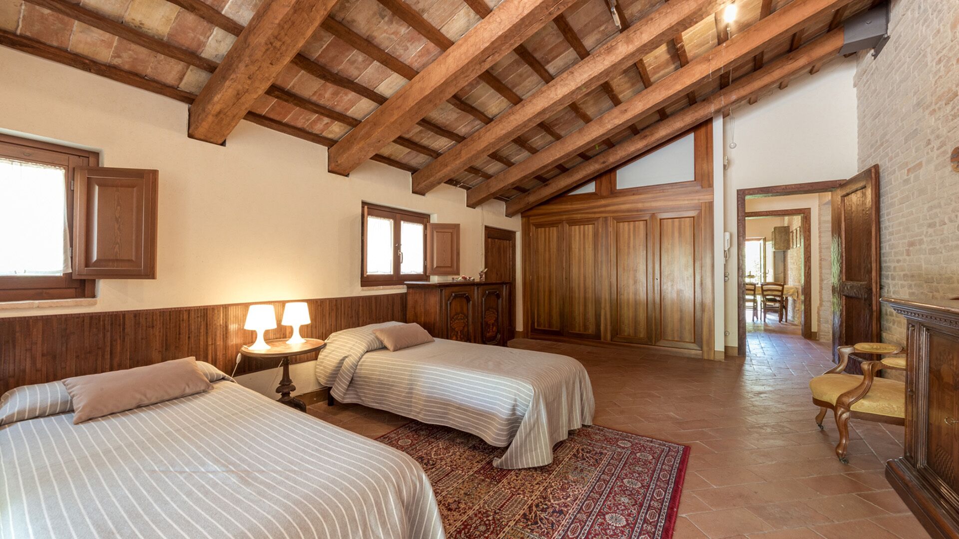 Una habitación con dos camas, vigas de madera, un armario grande de madera y vistas a un comedor.
