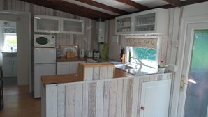 A compact kitchen with white cabinets, a microwave, a refrigerator, and a sink. - Beautiful river front self catering holiday lodge. (Builth Wells)