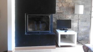 A room with a stone wall, a black fireplace, a white side table with a television, and a floor lamp. - Self catering El Rincon de Zaldierna for 4 people (Ezcaray)